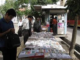 A group of people looking at a table of newspapers
AI-generated content may be incorrect.